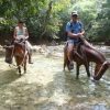 Deux personnes montant à cheval dans un ruisseau dans la jungle, naviguant dans une nature sauvage luxuriante et vibrante avec Salto La Jalda (randonnée et natation).